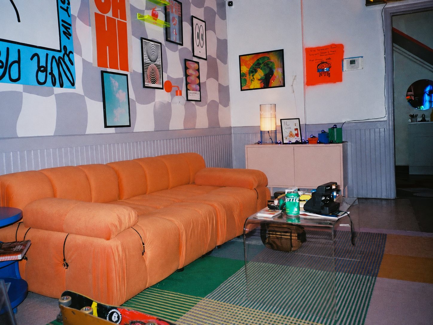 Lounge area with a checkered mural wall, gallery wall, and orange sofa