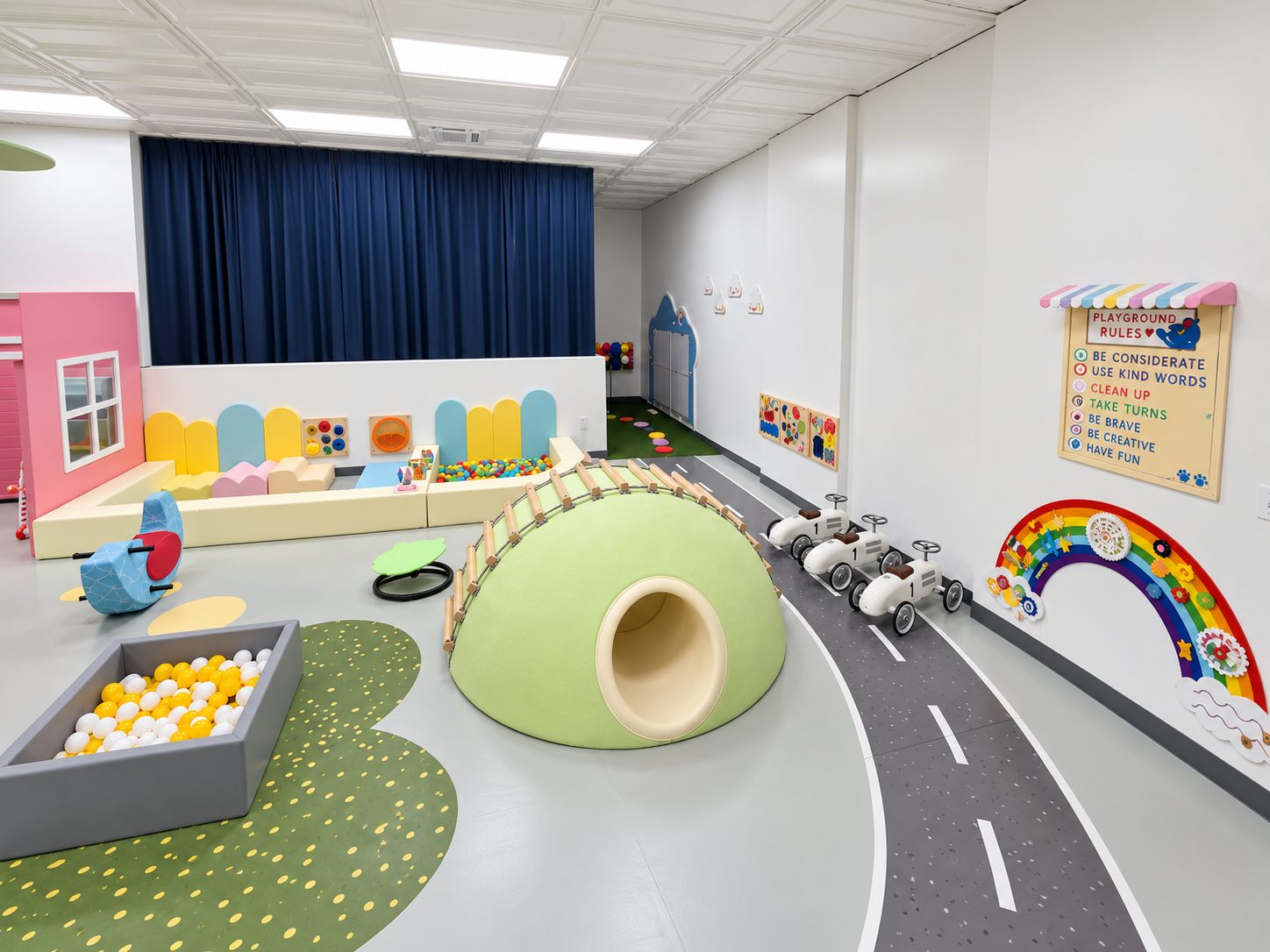 Stage area with a blue curtain, soft play shapes, and ride-on cars
