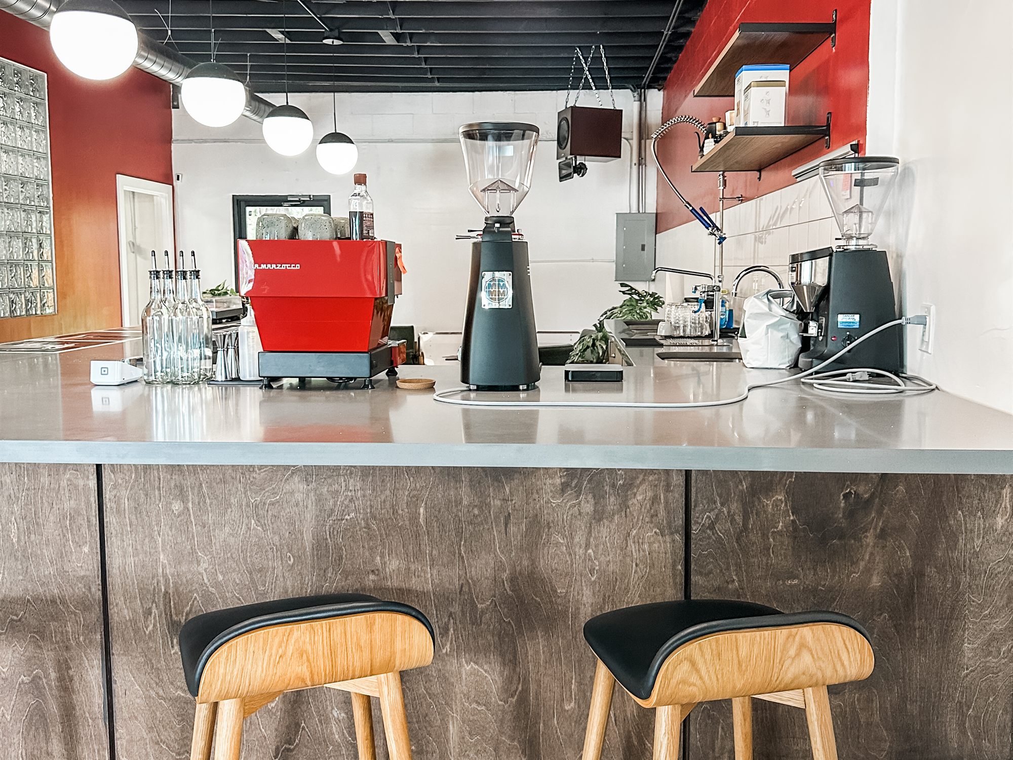 The completed Not Another Film Lab interior in Orlando, Florida: a long customer counter with stools, a red accent wall, and globe pendants under an exposed black ceiling