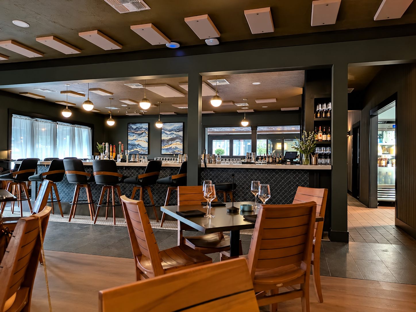 Main dining room with slatted wood chairs and the bar beyond