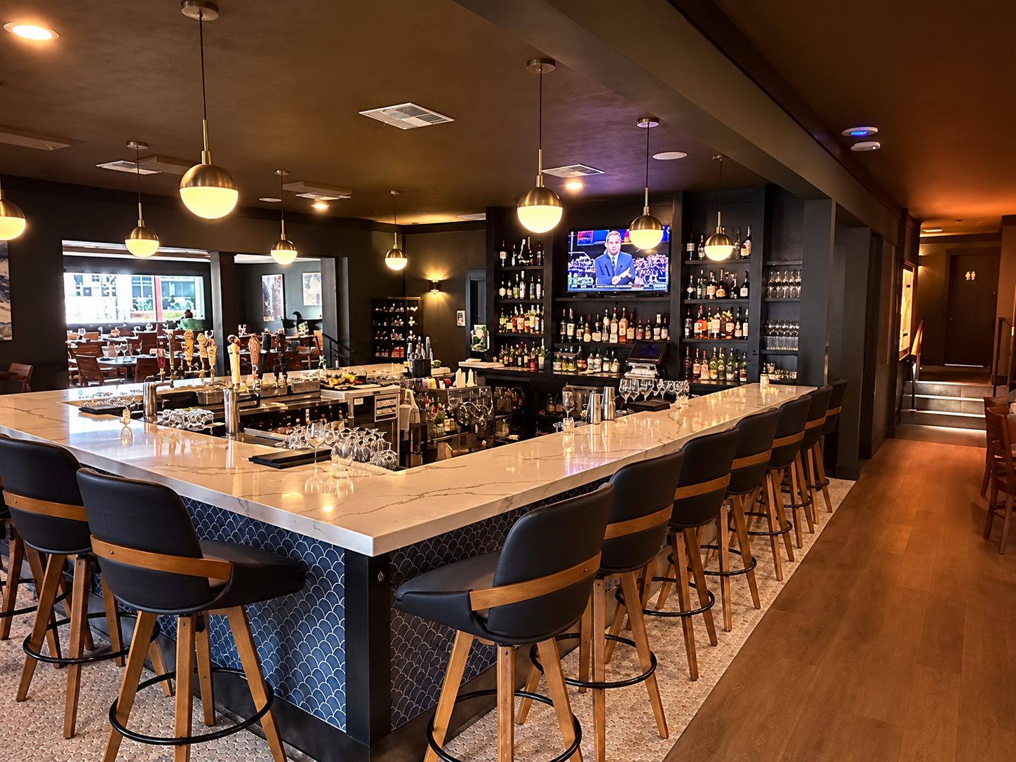 The bar with a white stone counter, blue scalloped tile base, and globe pendants