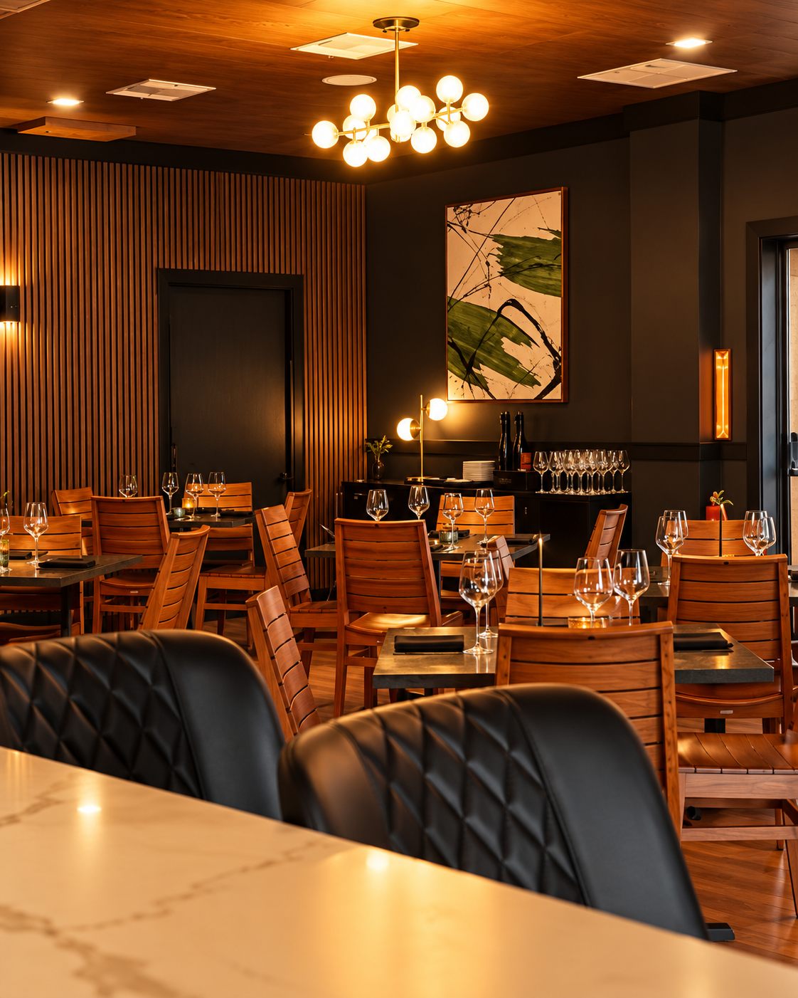 Dining room at Salt & Ember in Mount Dora, Florida, with a wood slat wall, banquette seating, and a globe chandelier